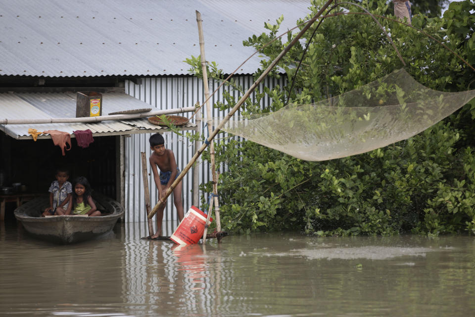 An Indian flood affected boy fishes as two children sit on a country boat near their partially submerged house in Gagolmari village, Morigaon district, Assam, India, Tuesday, July 14, 2020. Hundreds of thousands of people have been affected by floodwaters and landslides following incessant rainfall in the region. (AP Photo/Anupam Nath)