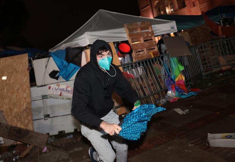 LOS ANGELES, CALIFORNIA - May 1: A pro-Israeli supporter takes an umbrella from a Pro-Palestinian encampment from at UCLA early Wednesday morning. (Wally Skalij/Los Angeles Times)