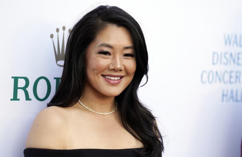 An Asian woman with long, dark hair smiling in a sleeveless black gown and a thin necklace.