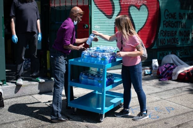 Water is handed out near an overdose prevention site in Vancouver’s Downtown Eastside on Tuesday. Municipalities like the City of Vancouver are updating their heat response plans after criticism. (Maggie MacPherson/CBC - image credit)