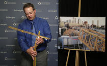 Brian Haight, crane program manager for Washington state's Department of Labor and Industries, uses a model of a crane to explain how a crane can become unstable after pins are removed and high winds come up as he talks about a crane collapse in Seattle months earlier that killed four, Thursday, Oct. 17, 2019, in Tukwila, Wash. The photo behind him shows broken off sections from the collapse. Washington state's L&I released the results of its investigation on the collapse Thursday. It found, as experts have long suspected, that the crane toppled because workers who were disassembling it had prematurely removed pins securing the sections of the crane's mast. (AP Photo/Elaine Thompson)