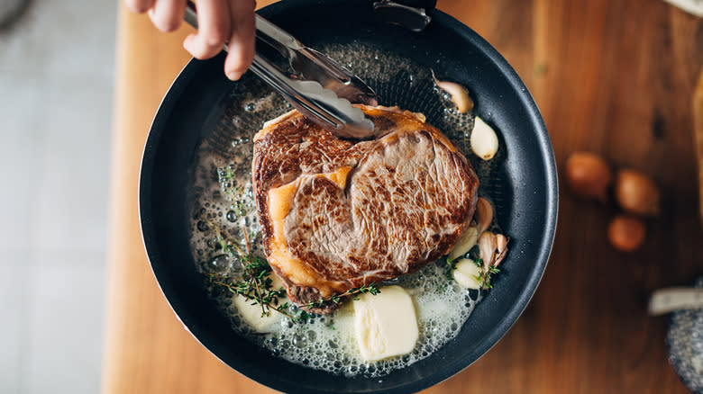 Person cooking steak in skillet