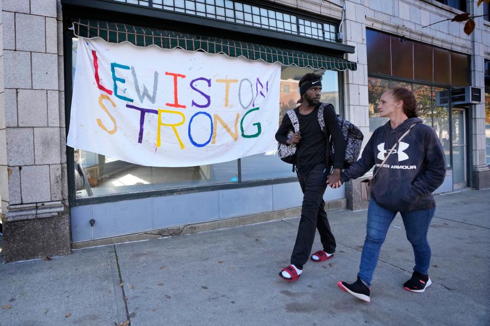 A couple walks by a banner that was put up in response to this week's deadly mass shootings, Friday, Oct. 26, 2023, in Lewiston, Maine. Police are still searching for the suspect who killed at least 18 in separate shootings at a bowling alley and restaurant on Wednesday. (AP Photo/Robert F. Bukaty)