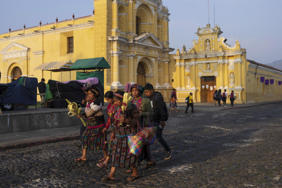 Mayan women walk past the San Pedro Catholic church, some carrying decorative palm frond crosses, at the start of Holy Week in Antigua, Guatemala, on Palm Sunday, March 24, 2024. (AP Photo/Moises Castillo)