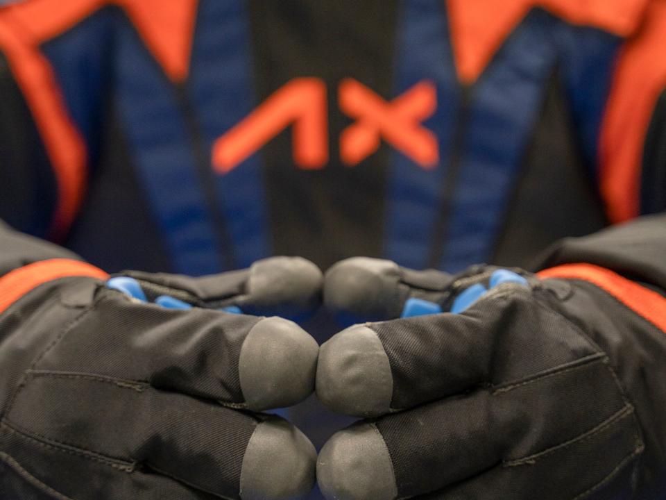 two hands in black space gloves touch fingers in front of black orange blue spacesuit