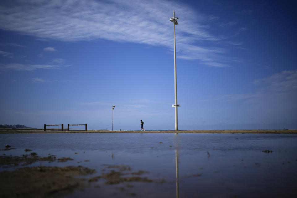 A runner passes by a large puddle of rainwater produced by a storm in Marseille, southern France, Thursday, Aug 18, 2022. (AP Photo/Daniel Cole)