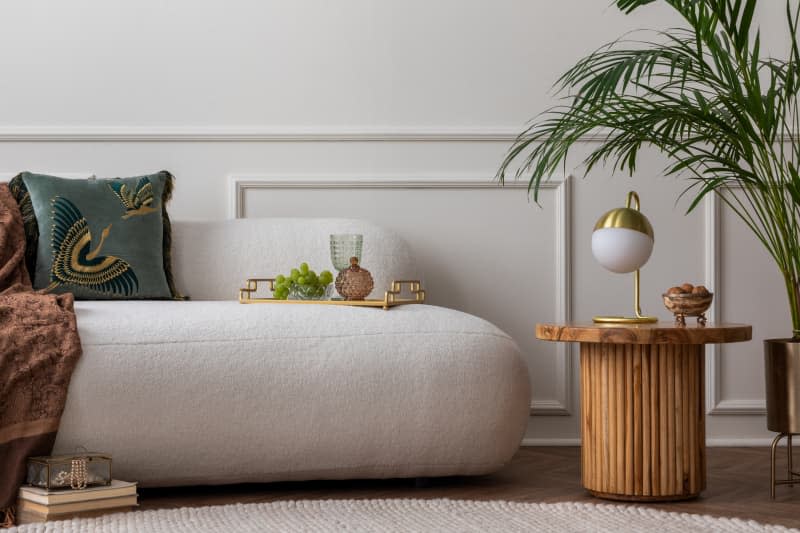 Art deco composition of living room interior with boucle sofa, plant, wooden coffee table, gold lamp, green pillow, elegant trace with glass, grape and personal accessories.