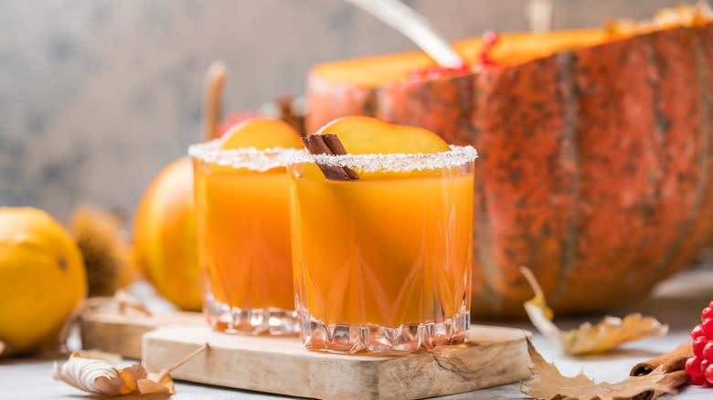 Cocktails with pumpkin in background and cinnamon sticks