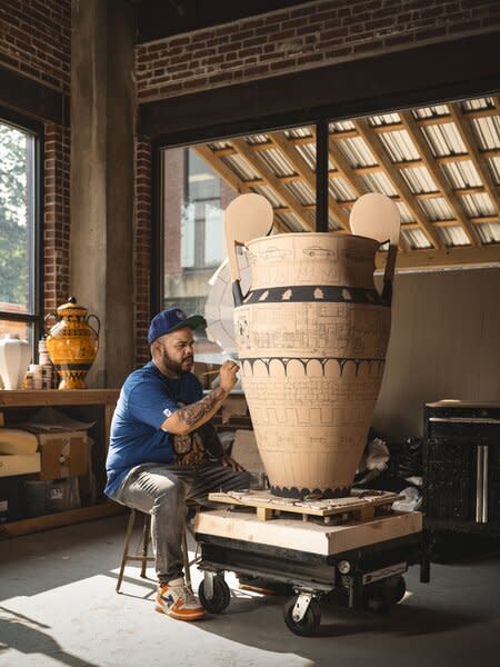 Lugo puts the final touches on one of his Orange and Black urns, inspired by the ancient Greco-Roman black- and red-figure vessels. Using this technique, the artist depicts specific narratives from his own childhood experience such as seeing a Black man get assaulted by a group of white supremacists, but also the overall realities of young black and brown people being unfairly targeted by the prison industrial complex.