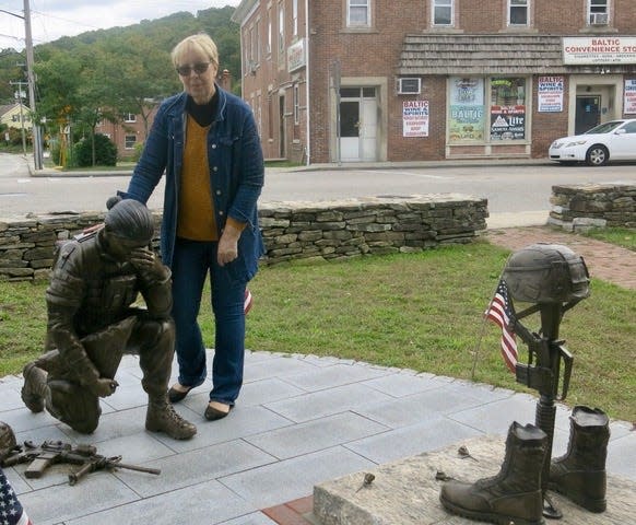 Connecticut Sen.  Cathy Osten, an Army veteran, stands next to a statue of a female combat veteran at Veterans Memorial Park in Sprague, Conn., in 2022.