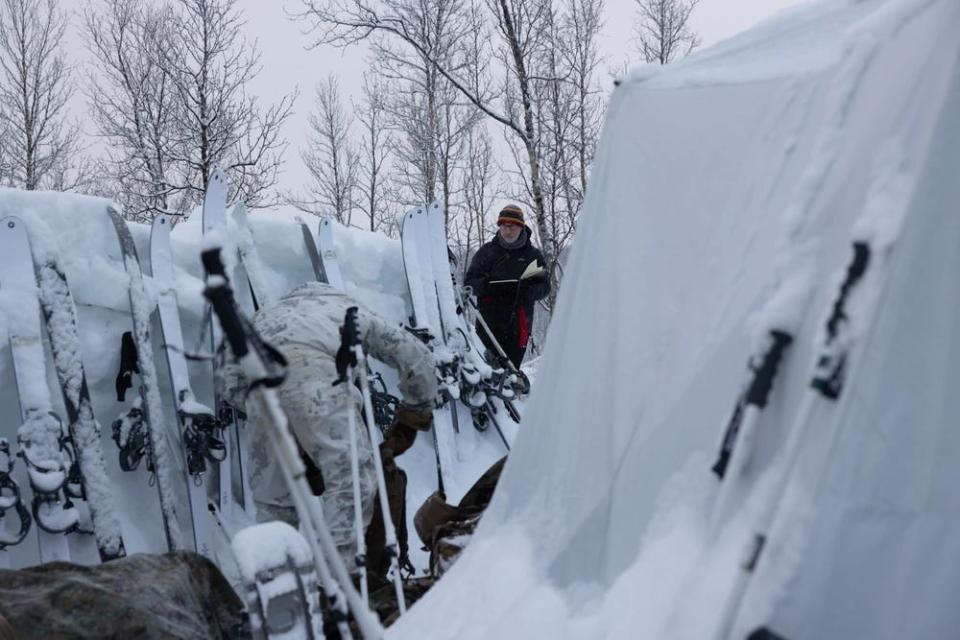 Richard Johnson, a combat artist, illustrates Marines during cold weather training behind a row of skis and equipment.