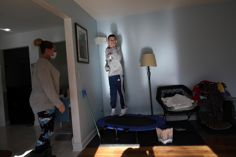 While paraprofessional Jessica Wein looks on, Josh Nazzaro bounces on a trampoline during a break from his remote learning at his home in Wharton, N.J., Wednesday, Nov. 18, 2020. The pandemic is threatening to wipe out the educational progress made by many of the nation’s 7 million students with disabilities. That's according to advocates, who say the extended months of learning from home and erratic attempts to reopen schools are deepening a crisis that began with the switch to distance learning in March. (AP Photo/Seth Wenig)