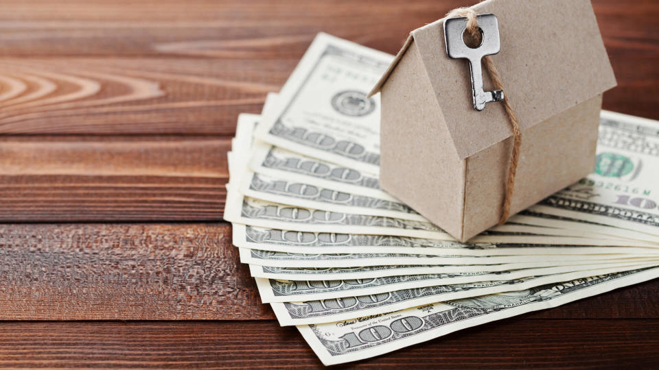 Model of cardboard house with key and dollar money.