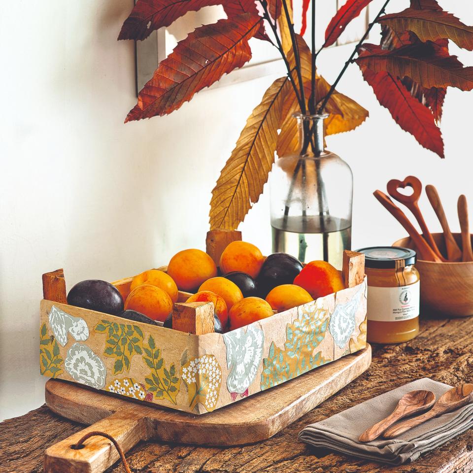 An autumn table setting with seasonal foliage in a vase and a crate of  fruit