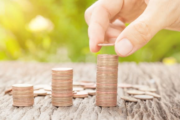 A hand putting another coin on a rising stack.