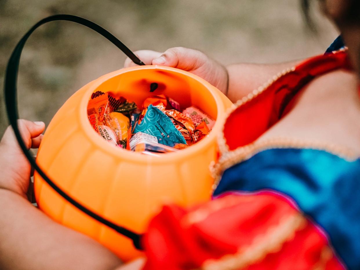 a child in Halloween costume holding a pumpkin bucket full of candy