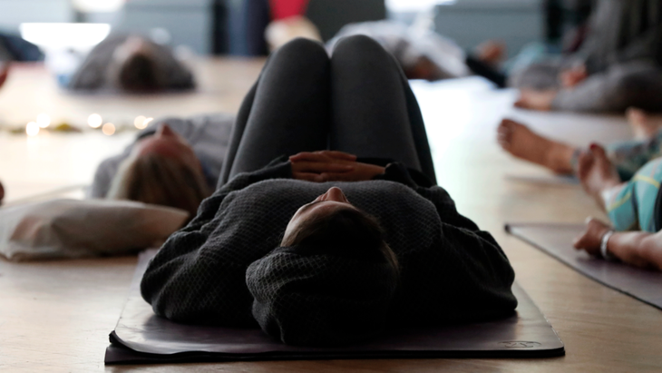 Woman lying down on her yoga mat with her knees together in a variation of Savasana during class led by a trauma-informed yoga teacher
