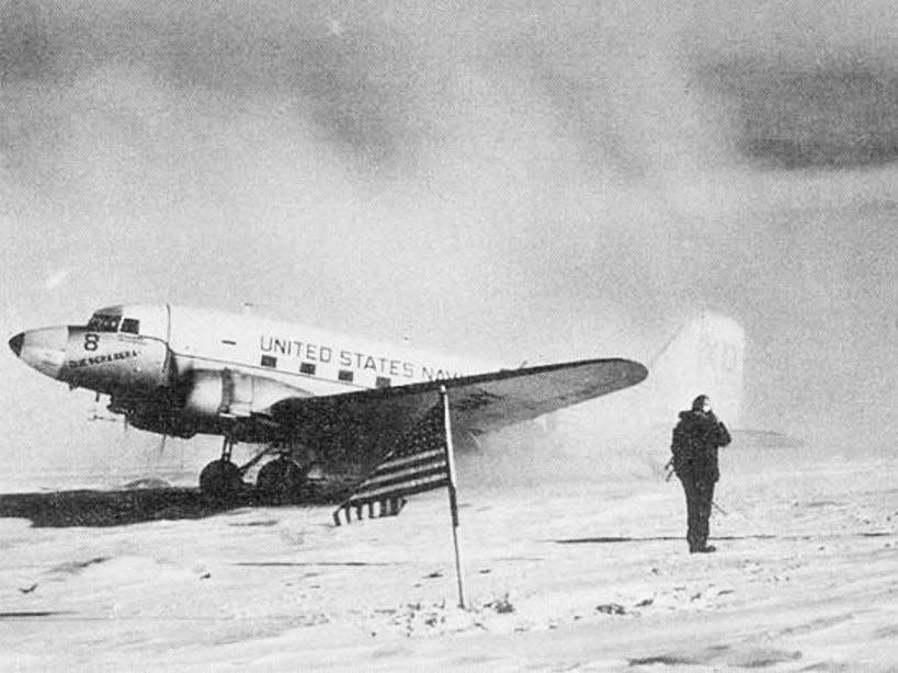 The R4D-5 Skytrain is parked at the South Pole behind the American flag after landing at the South Pole in 1956.