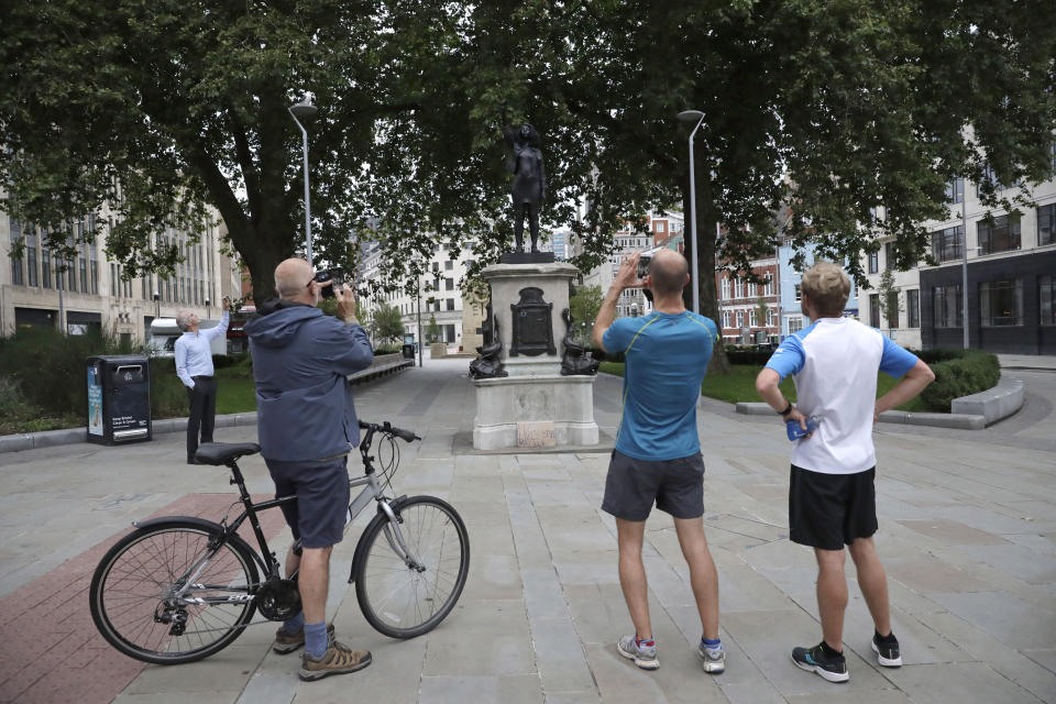 People look at a new black resin and steel statue entitled "A Surge of Power (Jen Reid) 2020" by artist Marc Quinn after it was put up this morning on the empty plinth of the toppled statue of 17th century slave trader Edward Colston, which was pulled down during a Black Lives Matter protest in Bristol, England, Wednesday, July 15, 2020. On June 7 anti-racism demonstrators pulled the 18-foot (5.5 meter) bronze likeness of Colston down, dragged it to the nearby harbor and dumped it in the River Avon — sparking both delight and dismay in Britain and beyond. (AP Photo/Matt Dunham)