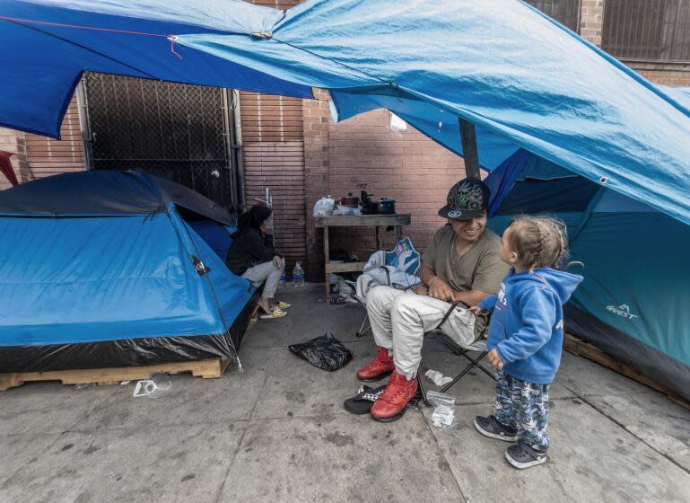 LOS ANGELES, CA - APRIL 25: Jhon (cq) Valencia plays with Thian, 2, with his mother Katherine Gonzalez in the back, on Towne Avenue in Skid Row. The county has said it was addressing the problem of families on the street and had the resources to house all families immediately but that has not happened. Photographed on Skid Row in Los Angeles, CA on Thursday, April 25, 2024. (Myung J. Chun / Los Angeles Times)