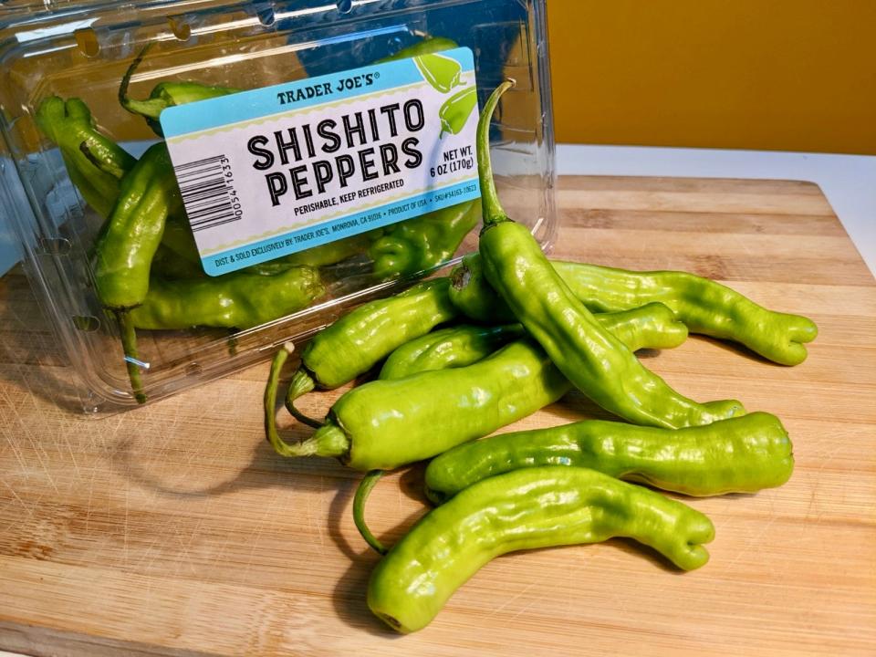 shishito peppers on a cutting board in front of a carton of trader joe's shishito peppers