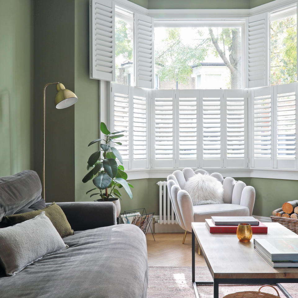 Living area with bay window, white shutters , green painted walls and white occasional chair