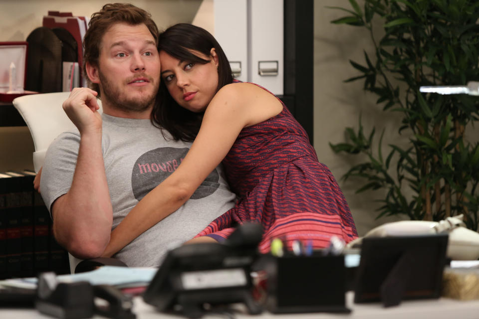 April Ludgate and Andy Dwyer sitting closely on a chair with April embracing Andy from behind in an office setting