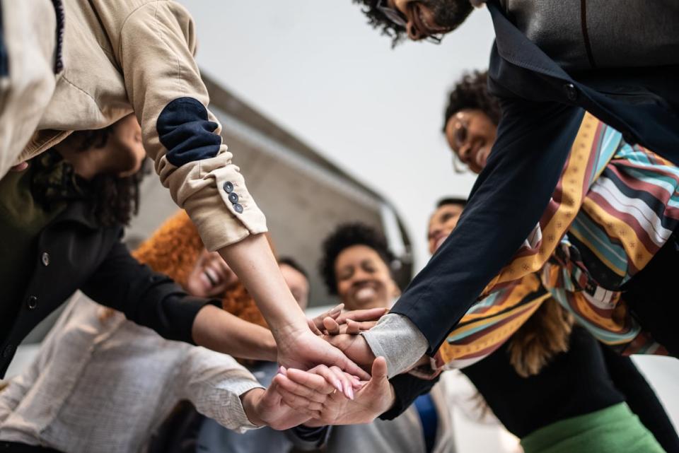 A smiling group of friends stack their hands to celebrate accomplishments.