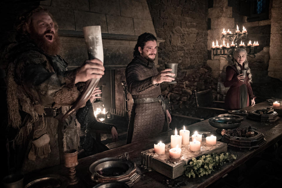 This image released by HBO shows Kristofer Hivju, from left, Kit Harington and Emilia Clarke in a scene from "Game of Thrones." fans got a taste of the modern world when eagle-eyed viewers spotted a takeout coffee cup on the table during a celebration in which the actors drank from goblets and horns. The characters Daenerys and Jon did not react to the out of place cup in Sunday’s episode. Many viewers complained the show should have caught the gaffe, which turned into an enduring meme on Monday.(Helen Sloan/HBO via AP)