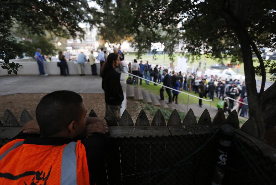 Worker pauses to look out over the infamous wooden picket fence atop the "Grassy Knoll" in Dealey Plaza towards a crowd of protestors chanting at the spot where the president was shot in Dallas
