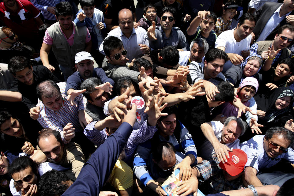 Iranians try to get ice-cream from Choopan dairy workers during a ceremony of unveiling 5-tons of ice-cream at the Tochal mountainous area of northern Tehran, Iran, Monday, April 1, 2013. Choopan dairy unveiled 5-tons of chocolate ice-cream, the largest in the world, according to the factory officials. (AP Photo/Ebrahim Noroozi)