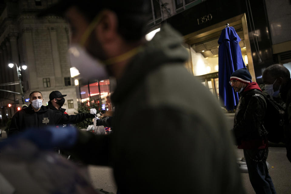 Hamza Deib, 28, left, owner of Taheni Mediterranean Grill, together with Mohammed Widdi, 31, coordinator of Muslims Giving Back, hand out food to the hungry as Aziz Almassoudi, 27, foreground, prepares the rest of the food packages in Herald Square, New York, on Monday, April 27, 2020. (AP Photo/Wong Maye-E)