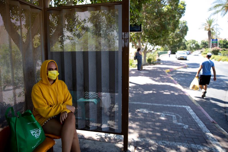 A woman wears a face mask as she sits at a bus stop in the Israeli settlement of Maale Adumim in the Israeli-occupied West Bank