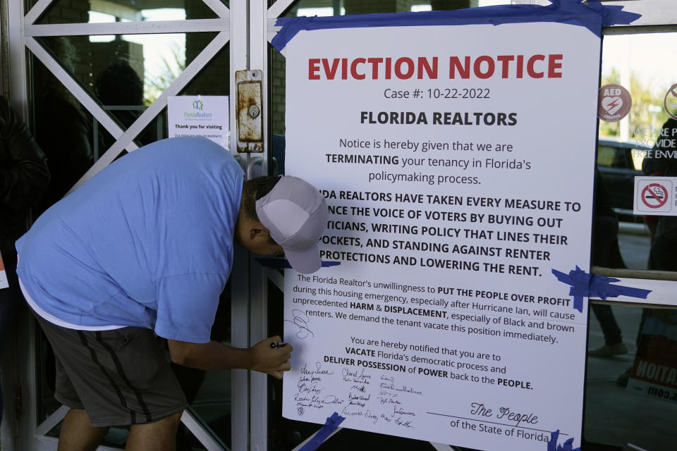 A rent control advocate signs his name to a mock eviction notice during a demonstration in front of the Florida Realtors office building Saturday, Oct. 22, 2022, in Orlando, Fla. (AP Photo/John Raoux)