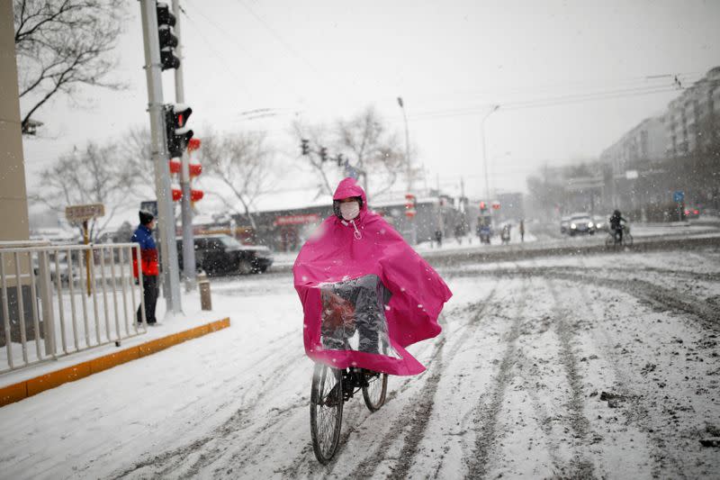 FILE PHOTO: Woman wearing a face mask rides a bicycle amid snow, as the country is hit by an outbreak of coronavirus, in Beijing