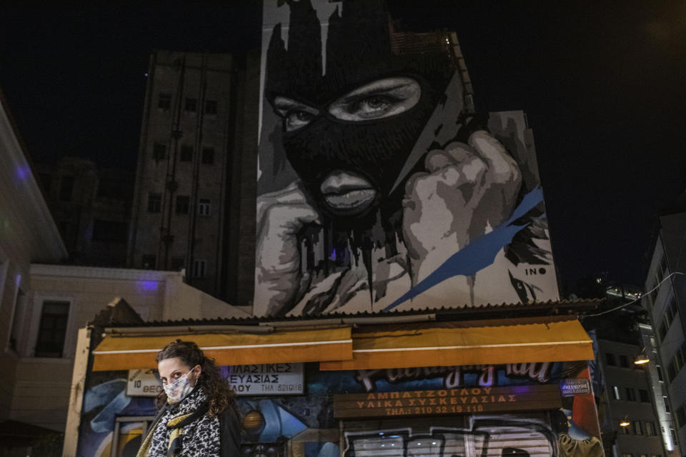 A woman wearing a face mask to curb the coronavirus walks in front of a mural created by street artist INO in the Psiri district of Athens, on Friday, Oct. 23, 2020. (AP Photo/Petros Giannakouris)