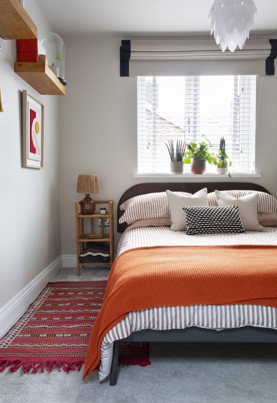 a guest bedroom in neutral colours with a grey upholstered bed frame and a bright orange bedspread