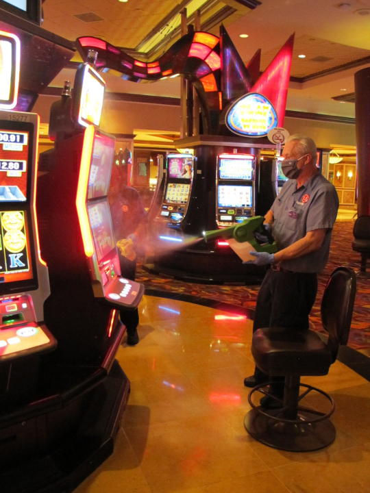 Steven Ford, a worker at Harrah's casino in Atlantic City, N.J., sprays slot machines with disinfectant Wednesday, July 1, 2020, as the casino prepared to reopen after 3 1/2 months of being shut down due to the coronavirus. Five of Atlantic City's casinos will reopen on Thursday, while three others, including Harrah's, will open Friday. (AP Photo/Wayne Parry)