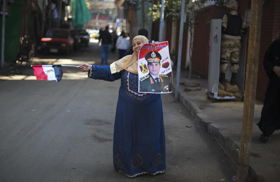 FILE - In this Wednesday, Jan. 15, 2014 file photo, an Egyptian woman dances in front of a polling station holding a poster of Egypt's Defense Minister, Gen. Abdel-Fattah el-Sissi, and a national flag in the second day of the vote in the country's constitutional referendum in Cairo, Egypt. Having secured victory in a referendum on a relatively liberal constitution that he championed, insiders say Egypt's military chief is turning his attention to the country’s overwhelming array of problems _ from health and education to government subsidies and investment. The revelations offer the latest indication that Gen. Abdel-Fattah el-Sissi is planning a run for president, capping a stunning transformation for the 59-year-old who started in the infantry.(AP Photo/Khalil Hamra, File)