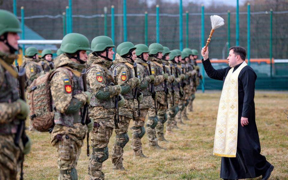  A priest sprinkles holy water during the graduation ceremony of the officers of the Armed Forces of Ukraine - Shutterstock