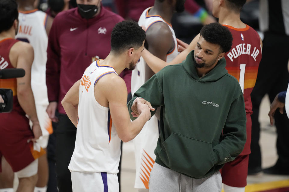 Phoenix Suns guard Devin Booker, left, shakes hands with injured Denver Nuggets guard Jamal Murray after the second half of Game 4 of an NBA second-round playoff series, Sunday, June 13, 2021, in Denver. Phoenix won 125-118 to sweep the series. (AP Photo/David Zalubowski)