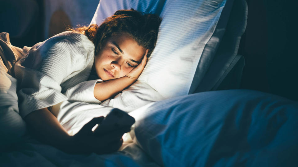 A woman scrolls on her phone in bed during the middle of the night