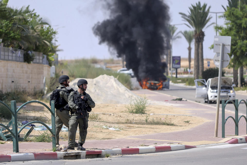 Israeli soldiers take position at the southern Israeli town of Ofakim on Sunday, Oct.8, 2023. Hamas militants stormed over the border fence Saturday, killing hundreds of Israelis in surrounding communities. The burning car was used by the gunmen and set on fire by the residents. (AP Photo/Ilan Assayag)