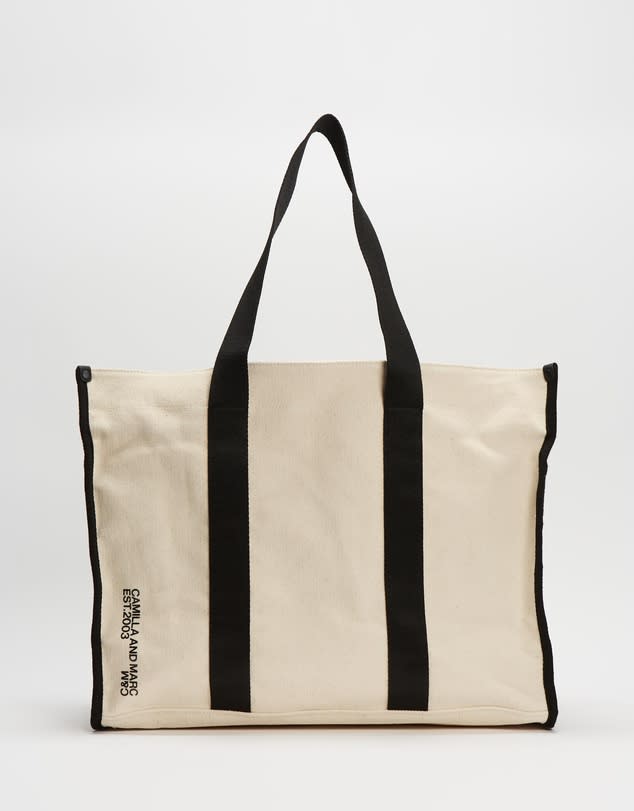 A white shopping tote with black piping and webbed handles. 