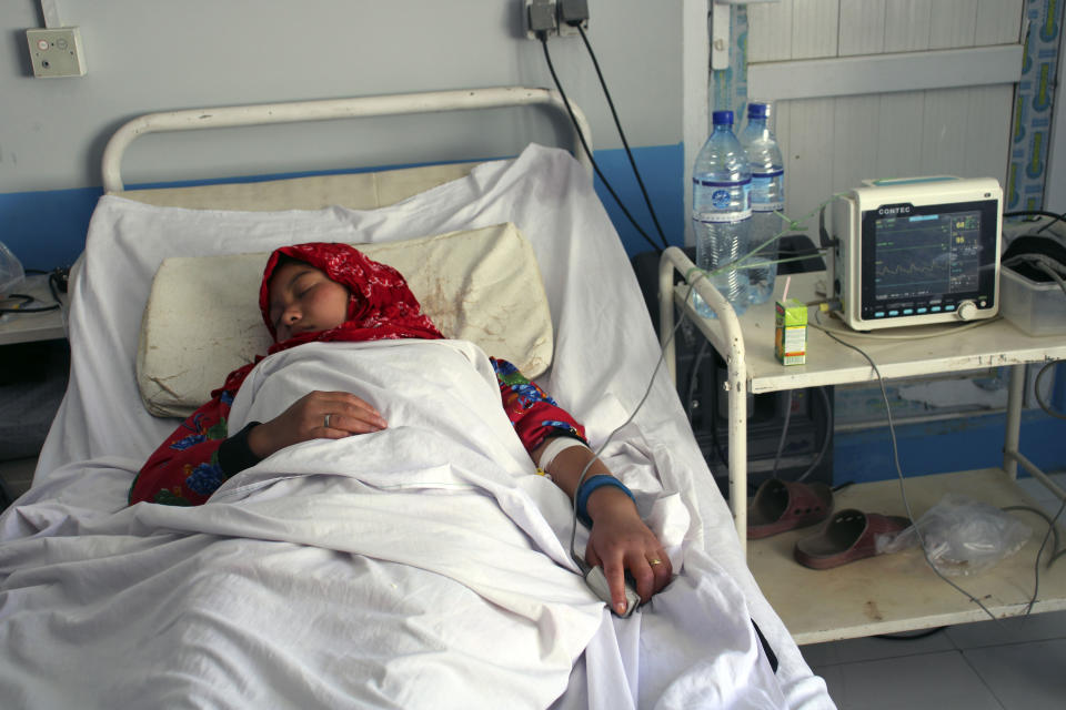 Someone wearing a red headscarf in a hospital bed connected to what appears to be a fingertip oxygen sensor.