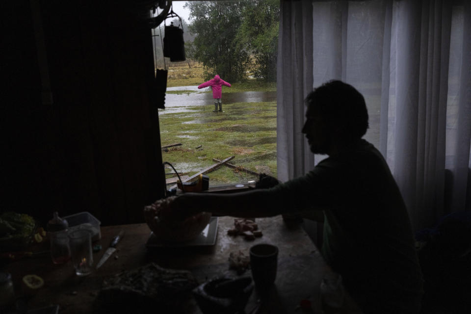 Likarayen Mariantu, the 9-year-old niece of Millaray Huichalaf, a Mapuche machi, or spiritual guide and healer, catches raindrops as a family friend helps prepare dinner at Huichalaf's home in Carimallin, southern Chile, on Tuesday, June 28, 2022. (AP Photo/Rodrigo Abd)
