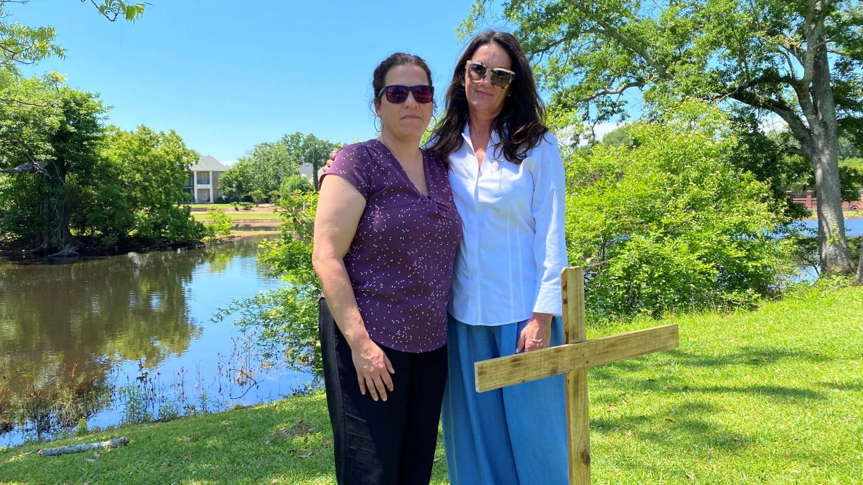 Sisters Hope Wise (left) and Cynthia Cayer stand near a cross for their brother, Donnie Cayer, who died near the spot on May 1, 2021, after he was hit by a driver who left the scene. The driver, David Brett Westmoreland, faces a trial in November.