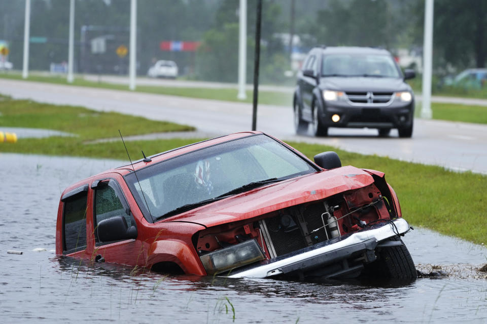 An abandoned vehicle is half submerged in a ditch next to a near-flooded highway