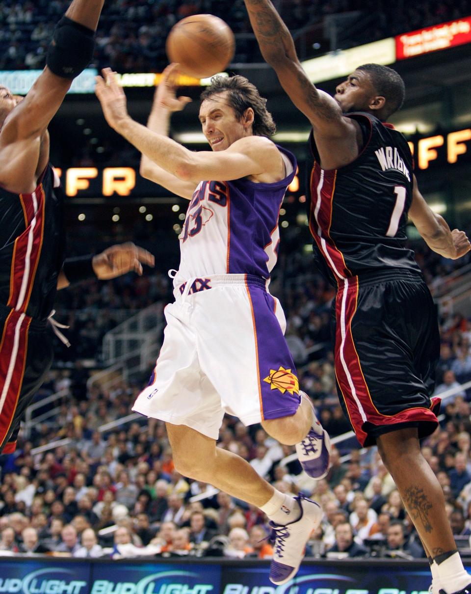 Phoenix Suns guard Steve Nash (13) passes around his back as Miami Heat forward Dorell Wright, right, and Alonzo Mourning, left, defend during the fourth quarter of an NBA basketball game Monday, Dec. 10, 2007 in Phoenix. The Heat won 117-113. (AP Photo/Matt York)