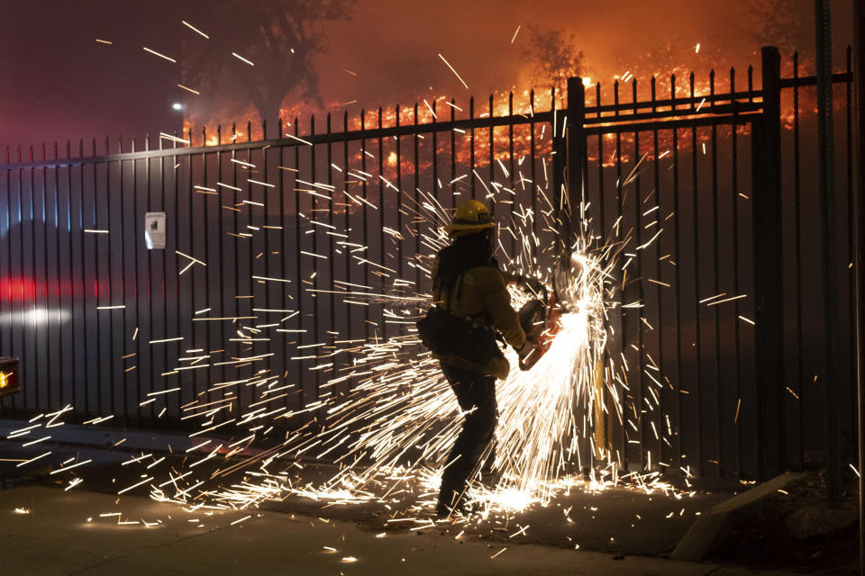 A firefighter cuts though a fence to gain access to the Saddleridge fire along Yarnell Street in Sylmar, Calif., Friday, Oct. 11, 2019. (David Crane/The Orange County Register via AP)